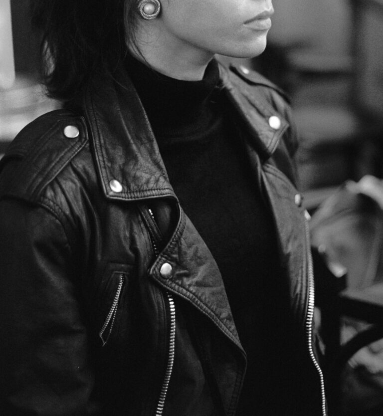 Home Black and white calm attractive female wearing stylish leather jacket standing on blurred interior of cafeteria and thoughtfully looking away